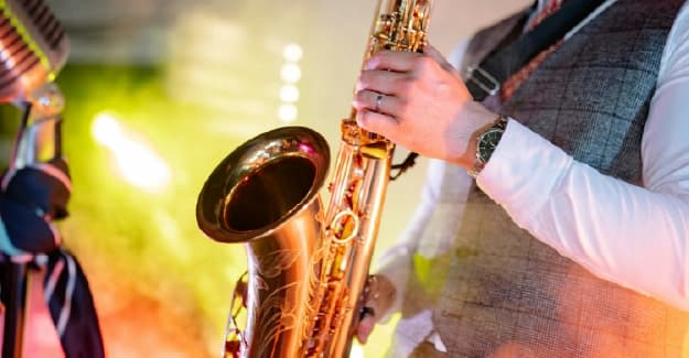 Músico tocando un saxofón dorado en primer plano durante un festival de jazz con luces cálidas.