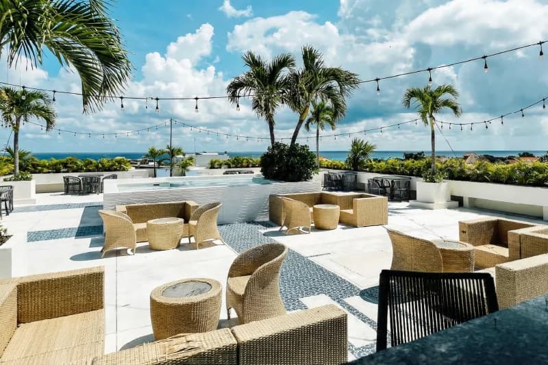 Terraza lounge en la azotea con sofás de mimbre, alberca pequeña y vistas al mar bajo el sol.