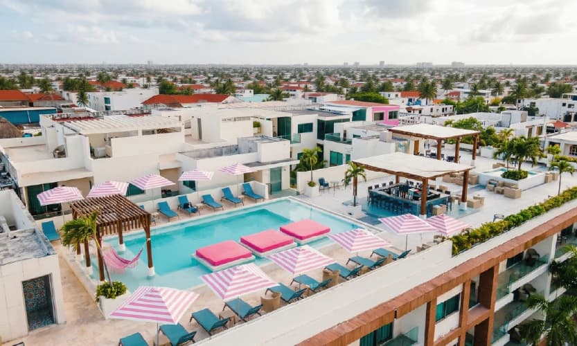 Alberca en azotea con camastros azules, sombrillas de rayas rosas y bar lounge con vista a la ciudad.